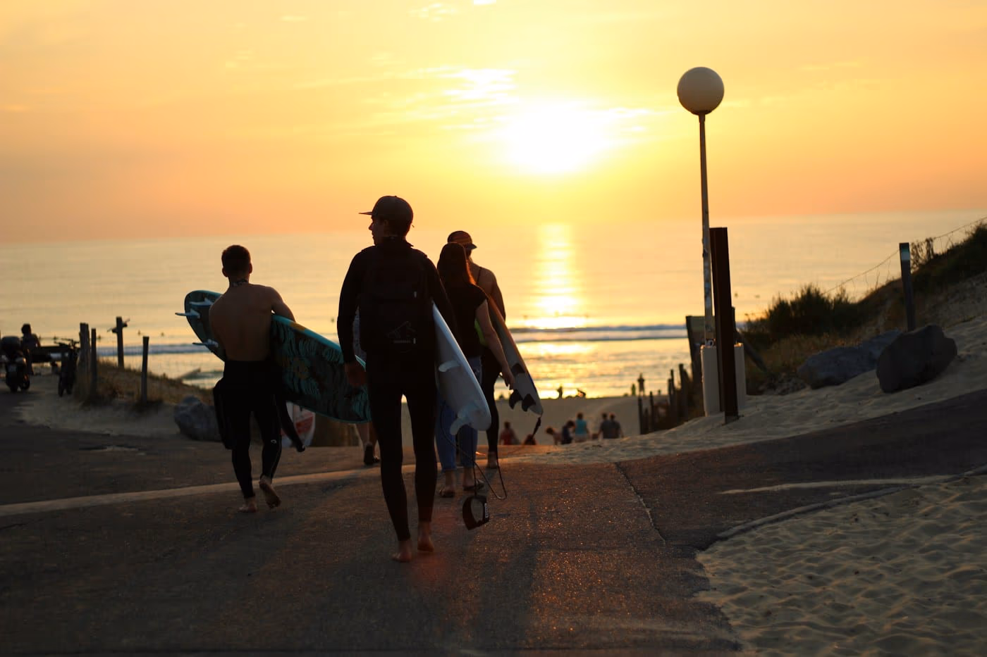 Surfeurs planche sous le bras qui reviennent de la plage au coucher du soleil