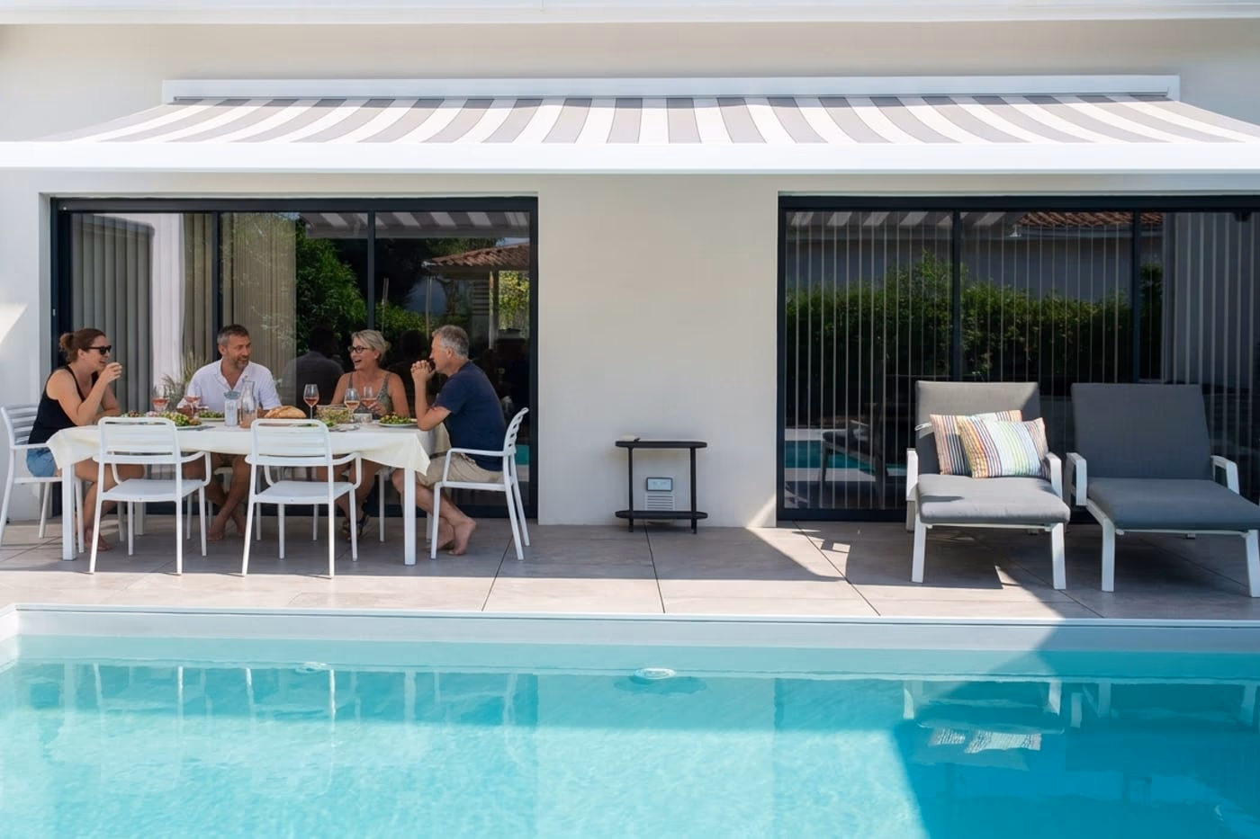 Amis qui déjeunent à l'ombre du store sur la terrasse, au bord de la piscine, maison Landes Habitat à Saint-Vincent-de-Paul (40)