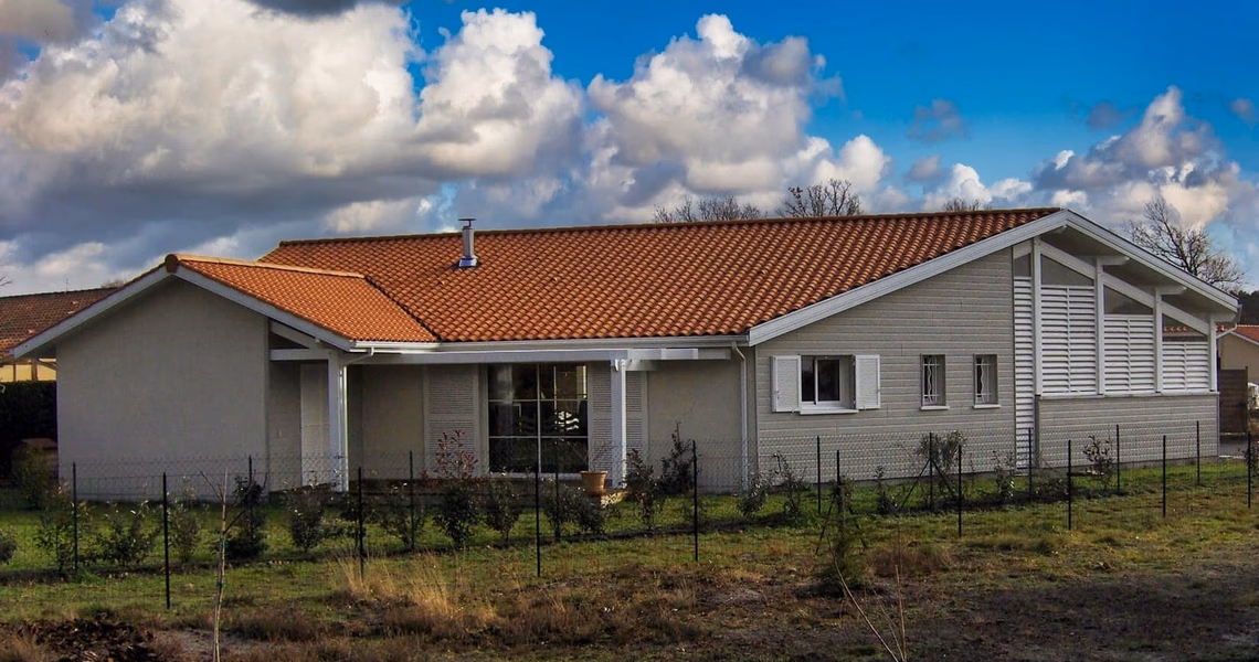 Maison de plain-pied à la façade claire avec un toit en tuiles oranges et un jardin clôturé.