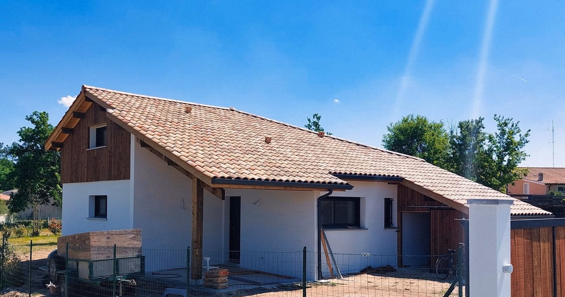 Façade d'une maison individuelle neuve en cours de finition avec toiture en tuiles et auvent en bois.