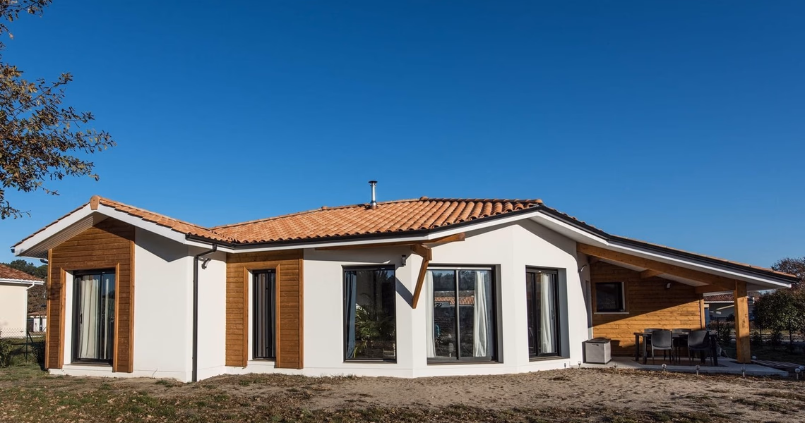 Façade blanche et bois d'une maison de plain-pied avec toiture en tuiles et terrasse couverte.