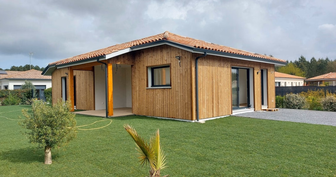 Maison individuelle de plain-pied avec bardage bois vertical, toiture en tuiles et terrasse couverte.