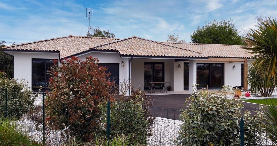 Maison individuelle de plain-pied aux murs blancs avec toiture en tuiles et menuiseries noires.