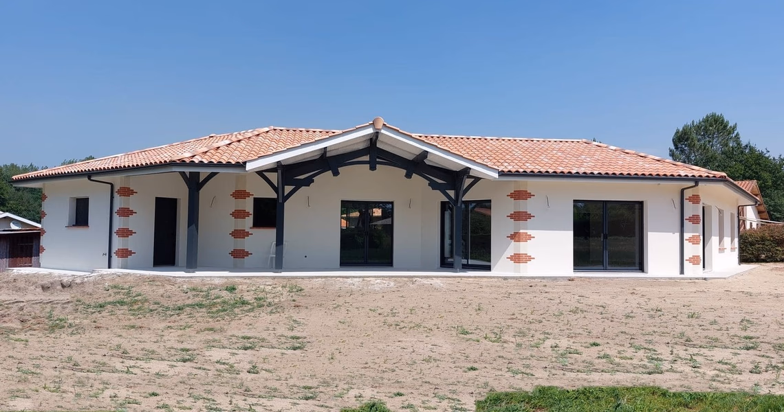 Façade avant d'une grande villa de plain-pied à toiture en tuiles rouges avec terrasse couverte.