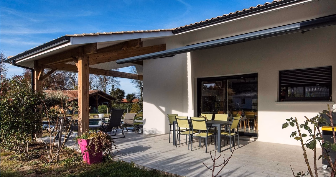 Grande terrasse carrelée avec table et chaises le long de la façade blanche d'une maison de plain-pied.