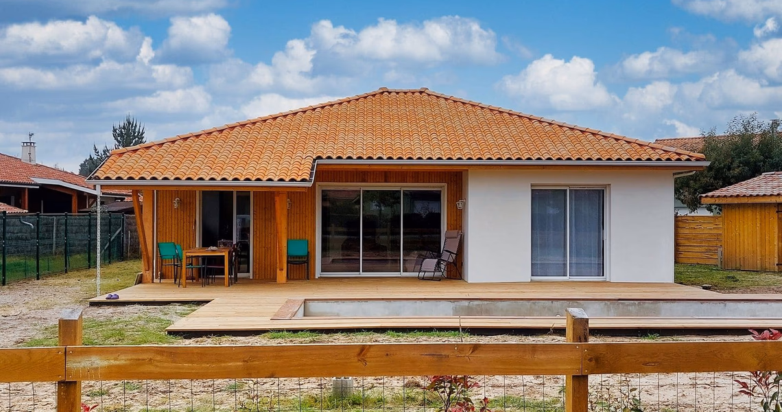 Façade arrière d'une maison de plain-pied avec toiture en tuiles, bardage bois, terrasse et piscine.