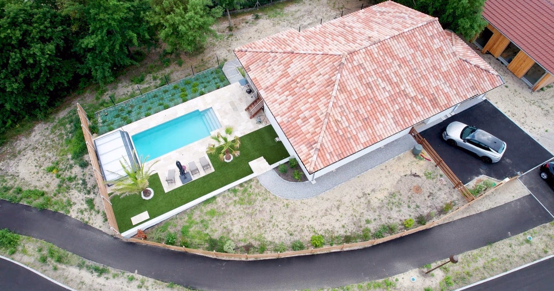Vue aérienne d'une maison de plain-pied avec toiture en tuiles, piscine, terrasse et pelouse synthétique.
