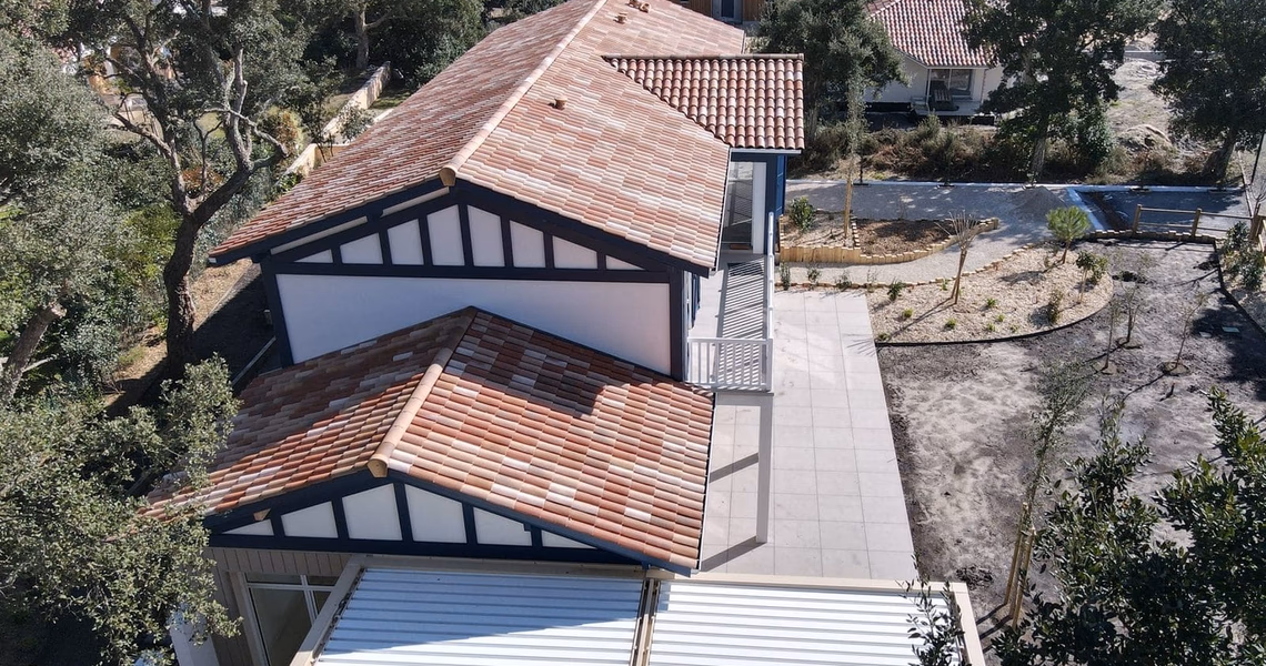 Vue aérienne d'une maison à toiture en tuiles rouges et colombages avec grande terrasse dallée.