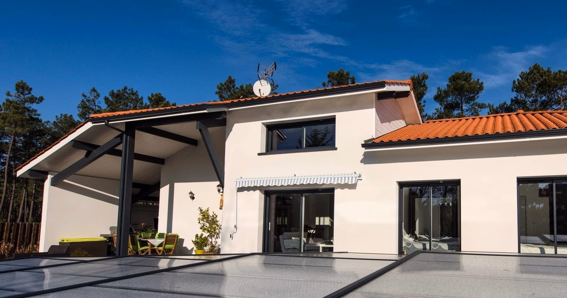 Façade blanche d'une maison à étage avec toiture en tuiles, grandes baies vitrées et abri de terrasse.