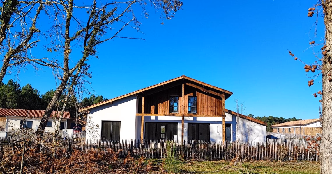 Façade principale d'une maison contemporaine en bois et enduit blanc sous un ciel bleu.