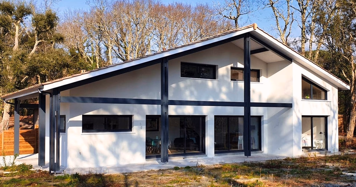 Villa contemporaine blanche à étage avec charpente métallique apparente et grandes baies vitrées.