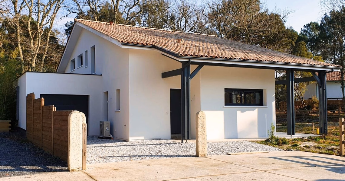 Façade de la villa moderne avec enduit blanc, toiture en tuiles, carport ouvert et allée en gravier.