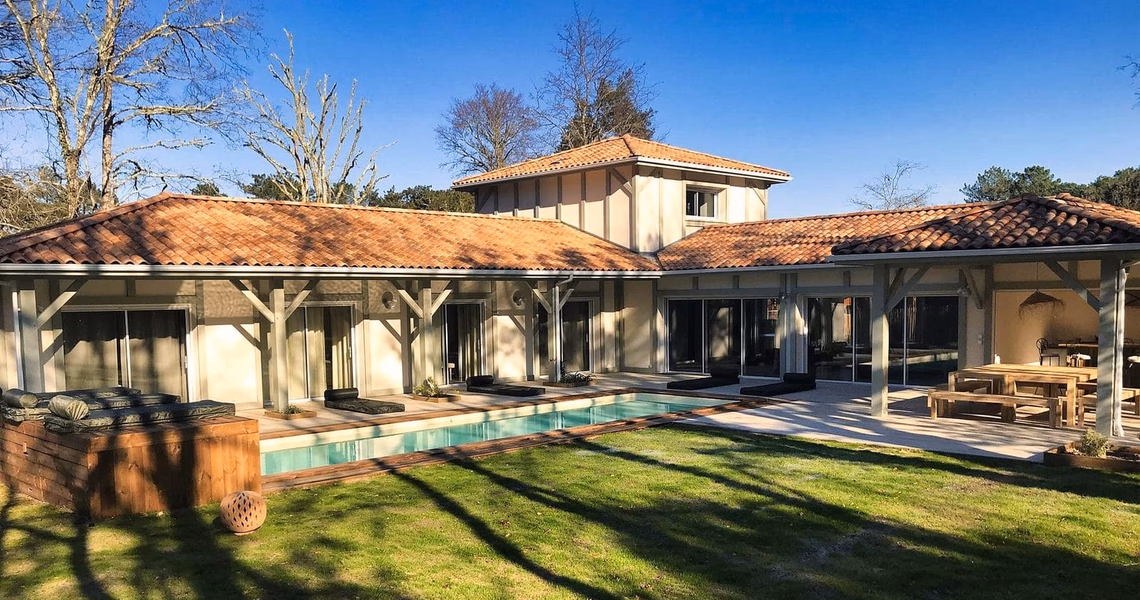 Façade arrière d'une maison landaise avec toiture en tuiles, piscine rectangulaire et terrasse en bois.