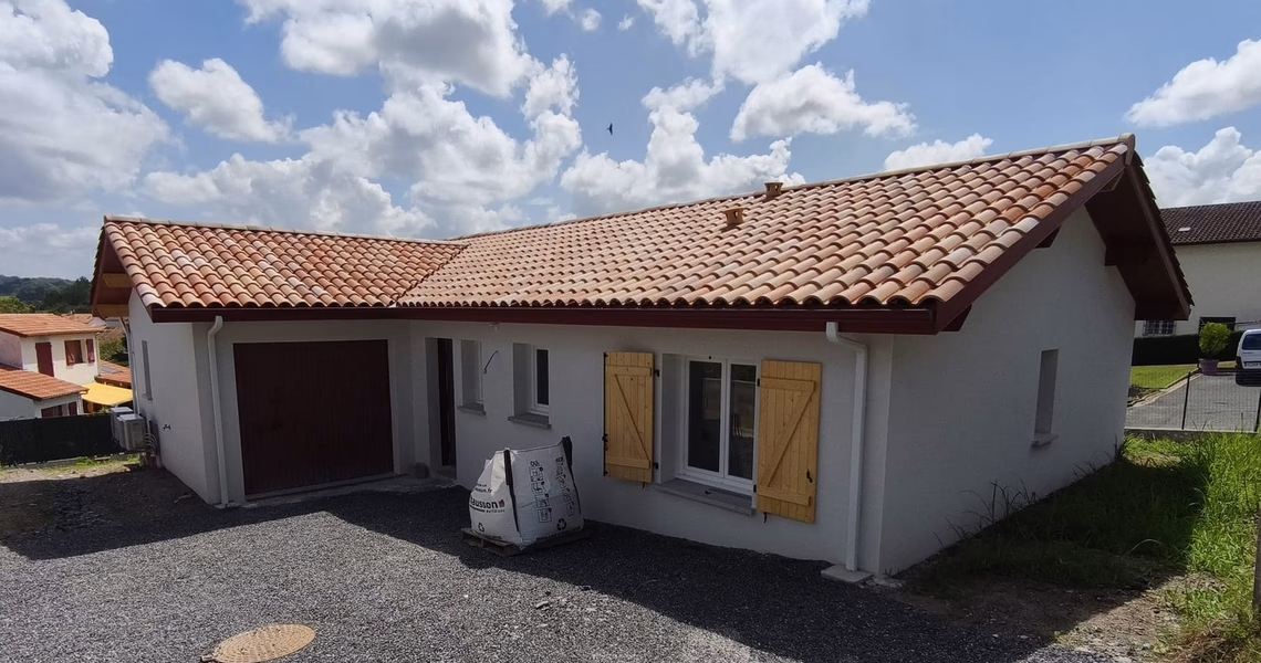 Façade avant d'une maison de plain-pied avec toiture en tuiles canal, volets en bois et graviers.