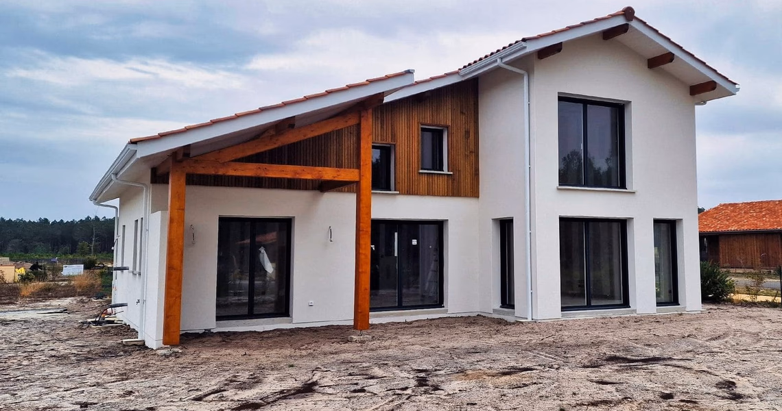 Maison individuelle R+1 à enduit blanc, bardage bois partiel, toiture en tuiles et grand porche en bois.