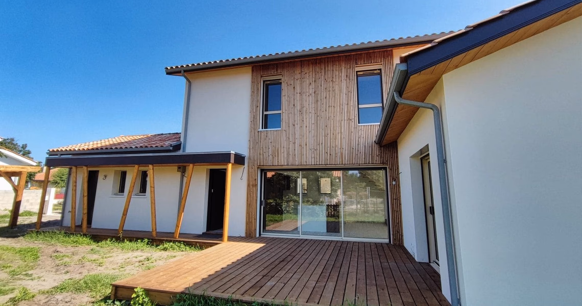 Façade de villa contemporaine à étage combinant enduit clair et bardage bois vertical avec terrasse en bois.