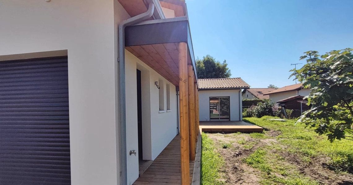 Façade de la villa contemporaine avec enduit clair, avancée de toit en bois et terrasse en L.