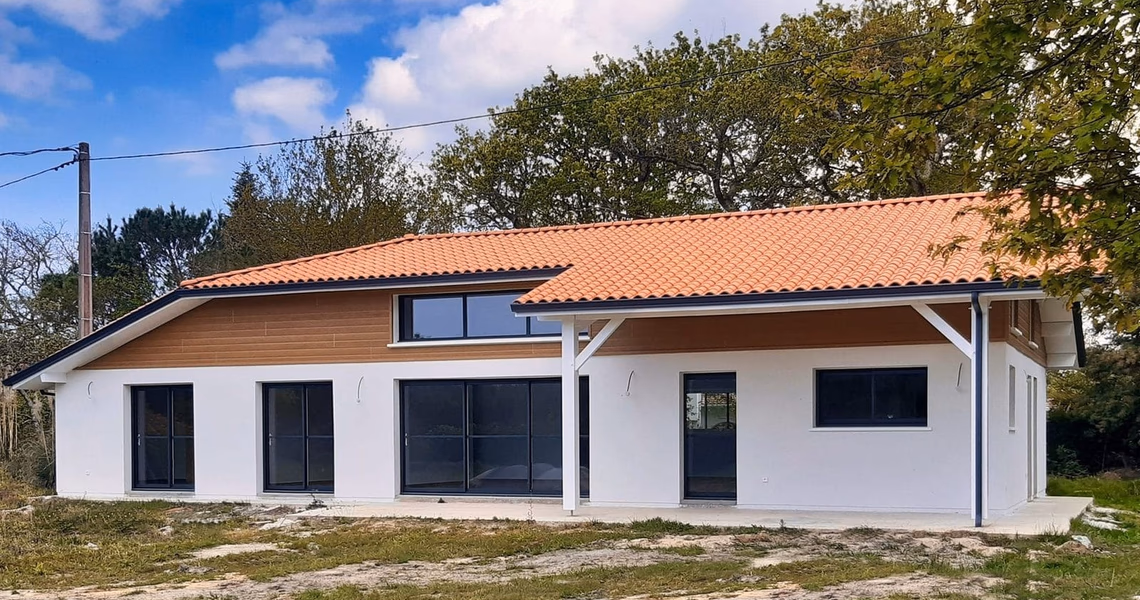 Façade arrière de la maison avec enduit blanc, bardage bois, grandes baies vitrées et toiture en tuiles.