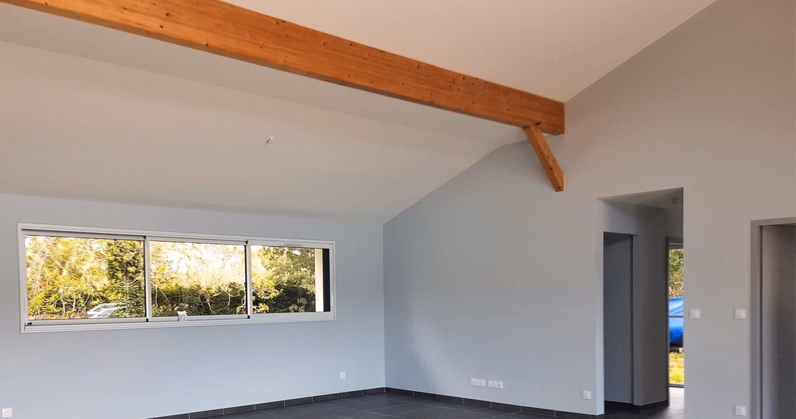 Grand salon lumineux avec une grande poutre en bois apparente sous la pente du toit.