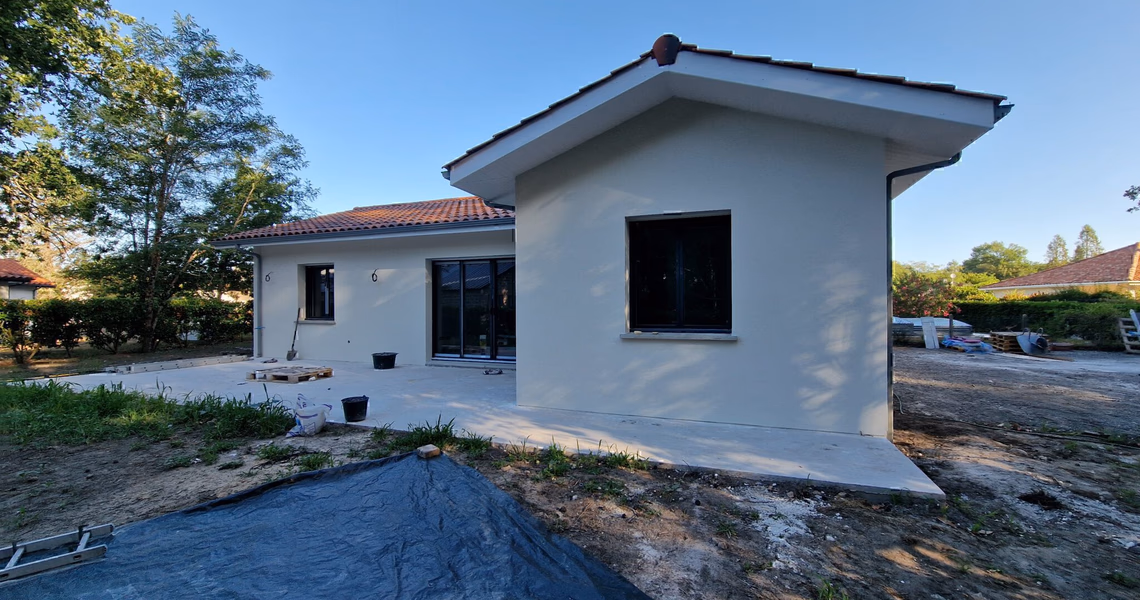 Façade arrière en angle avec dalle terrasse et grande baie vitrée aluminium ouvrant sur le jardin à Herm