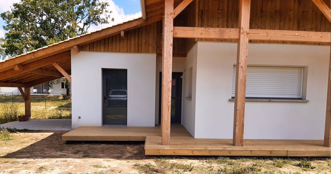 Façade de maison contemporaine enduite de blanc avec bardage bois et terrasse en bois surélevée.