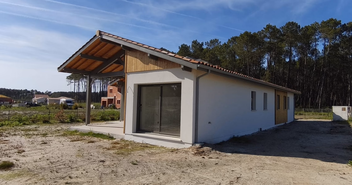 Maison moderne de plain-pied avec façade blanche, grande baie vitrée et porche en bois sous un ciel bleu.