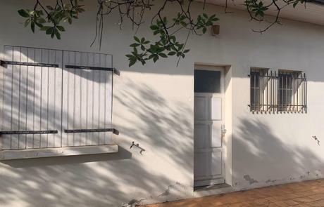 Façade d'une maison avec une porte blanche et des fenêtres à volets en bois.