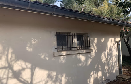 Mur extérieur d'une maison avec des fenêtres protégées par des grilles en métal.
