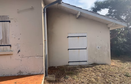 Mur extérieur d'une maison avec une porte blanche et des volets en bois fermés.