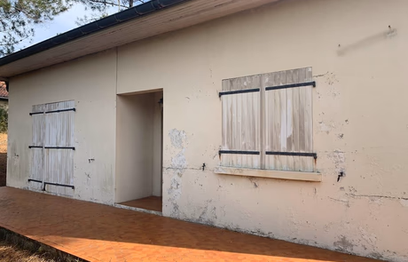 Mur extérieur d'une maison avec des fenêtres en bois fermées et un chemin en pavés.