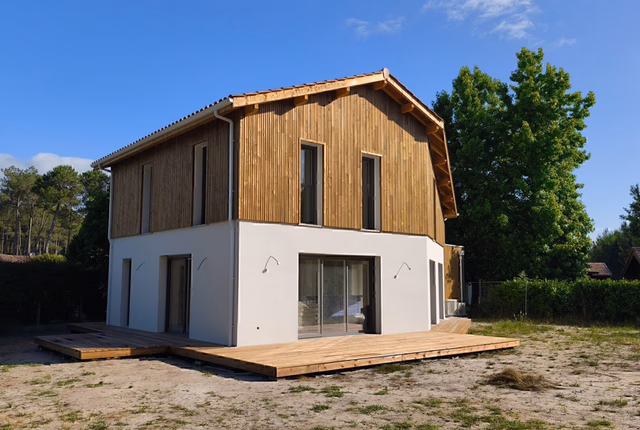 Maison individuelle à étage avec bardage bois à l'étage, rez-de-chaussée blanc et terrasse en bois.