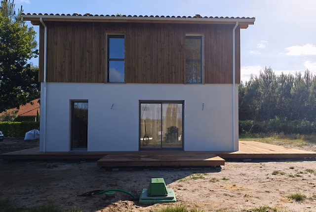 Façade arrière d'une maison à étage avec bardage bois à l'étage, rez-de-chaussée blanc et grande terrasse en bois.