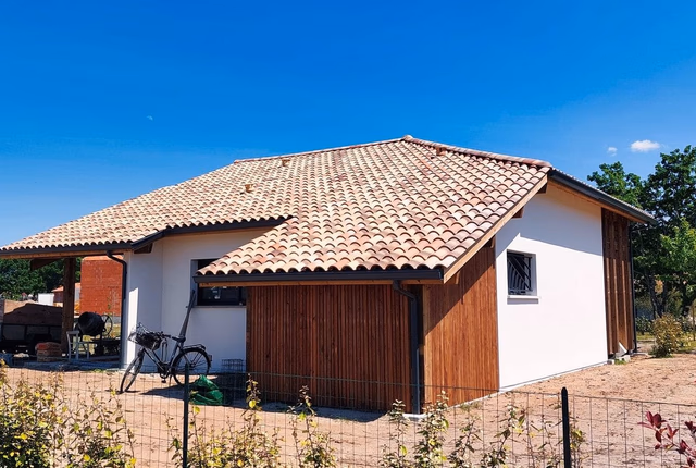 Façade arrière d'une maison de plain-pied avec toiture en tuiles et bardage en bois vertical.
