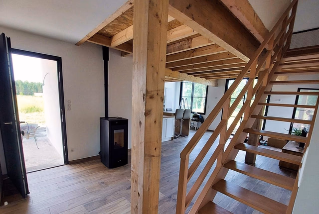 Intérieur de la maison avec poêle à granulés noir, sol carrelé imitation bois et escalier en bois.