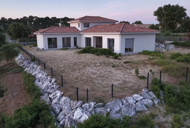 Villa contemporaine blanche à étage avec toiture en tuiles rouges sur un terrain en pente.