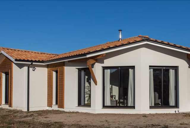 Façade de maison de plain-pied avec enduit blanc, habillage en bois et toiture en tuiles canal.