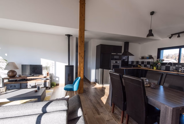 Grand espace de vie lumineux avec salon, poêle à bois et cuisine ouverte équipée avec coin repas.