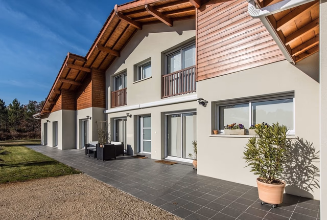 Façade arrière d'une grande villa contemporaine avec bardage bois, larges baies vitrées et terrasse carrelée.