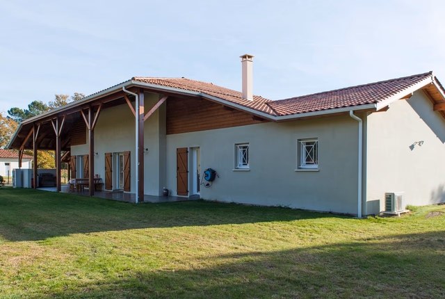 Façade arrière d'une maison avec toit en tuiles, grande terrasse couverte et jardin en pelouse.