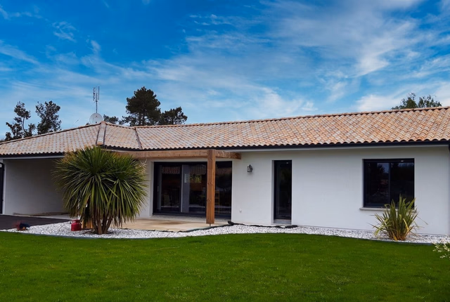 Maison de plain-pied blanche à toiture en tuiles avec menuiseries noires et jardin engazonné.