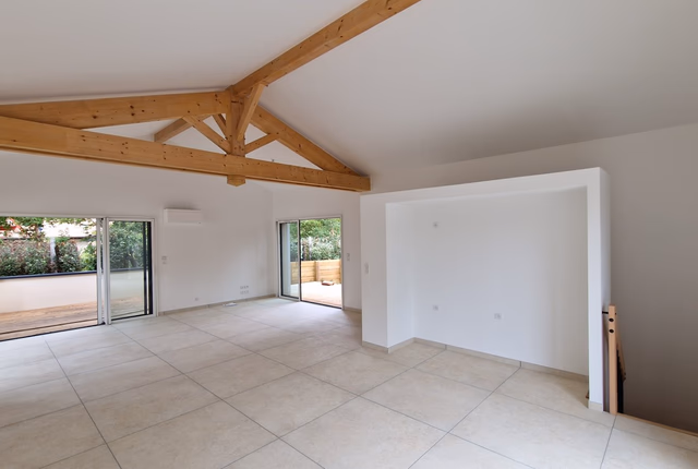 Grand salon lumineux sous charpente bois apparente avec sol carrelé et larges baies vitrées coulissantes.