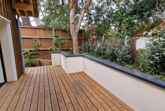 Terrasse en bois avec muret blanc et chapeau anthracite, ouverte sur un jardin arboré.
