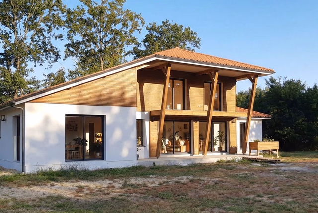 Façade de maison moderne à étage avec enduit blanc, bardage bois, toiture en tuiles et grand porche.