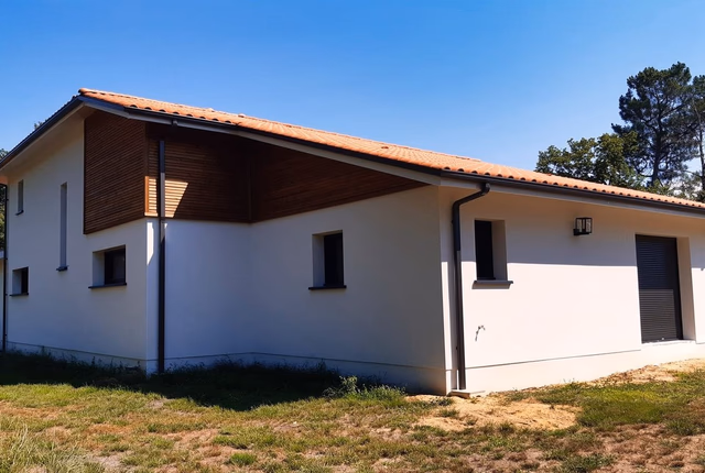 Maison moderne avec façade blanche, toiture en tuiles orange, parement en bois et fenêtres sombres.