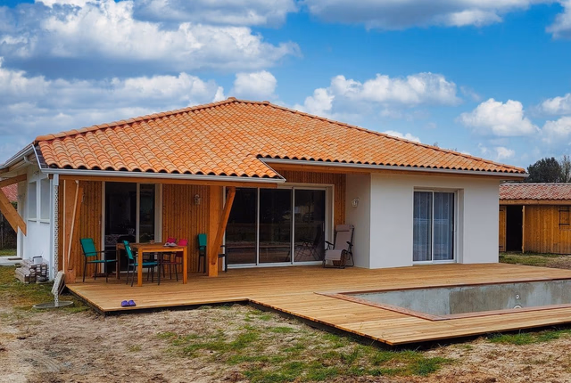 Maison de plain-pied avec toit en tuiles, bardage bois, grande terrasse et piscine en construction.