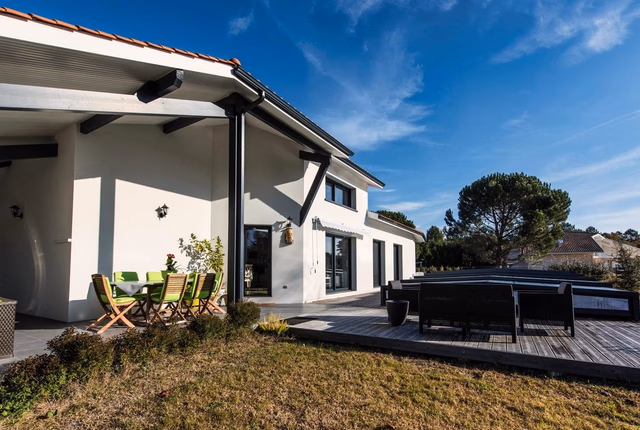 Façade blanche d'une maison moderne avec terrasse en bois, mobilier de jardin et pergola.
