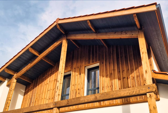 Gros plan sur la charpente en bois et le bardage vertical d'une villa avec deux fenêtres.