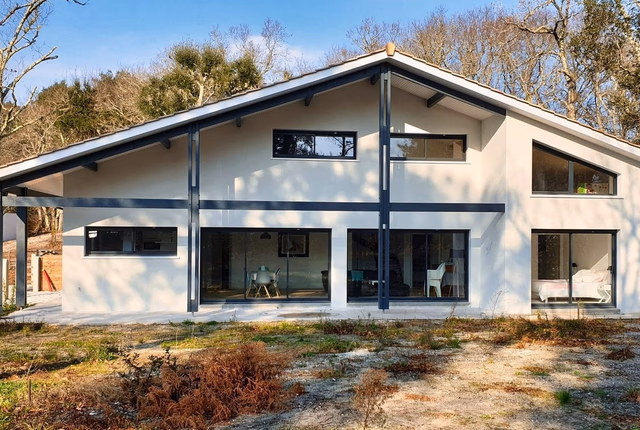 Façade arrière d'une grande maison moderne à étage avec enduit clair et menuiseries sombres.