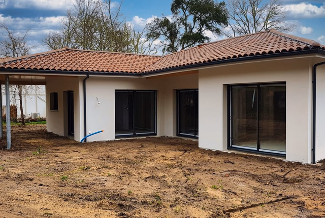 Façade arrière d'une villa de plain-pied avec toiture en tuiles romanes et grandes baies vitrées.