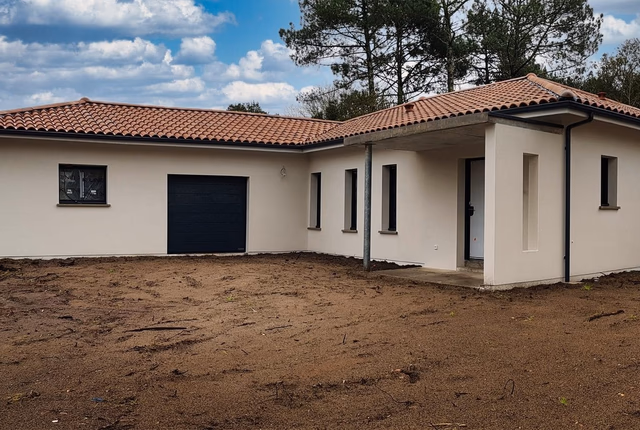 Façade d'une maison de plain-pied aux murs clairs, toiture en tuiles et grand terrain de terre.